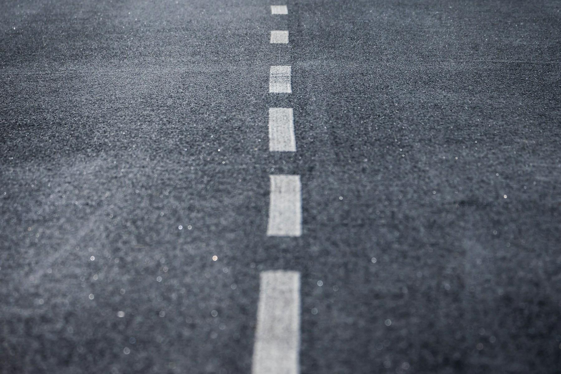 Unterbrochene weiße Mittellinie auf grauem Asphalt, flach von der Fahrbahn aus fotografiert