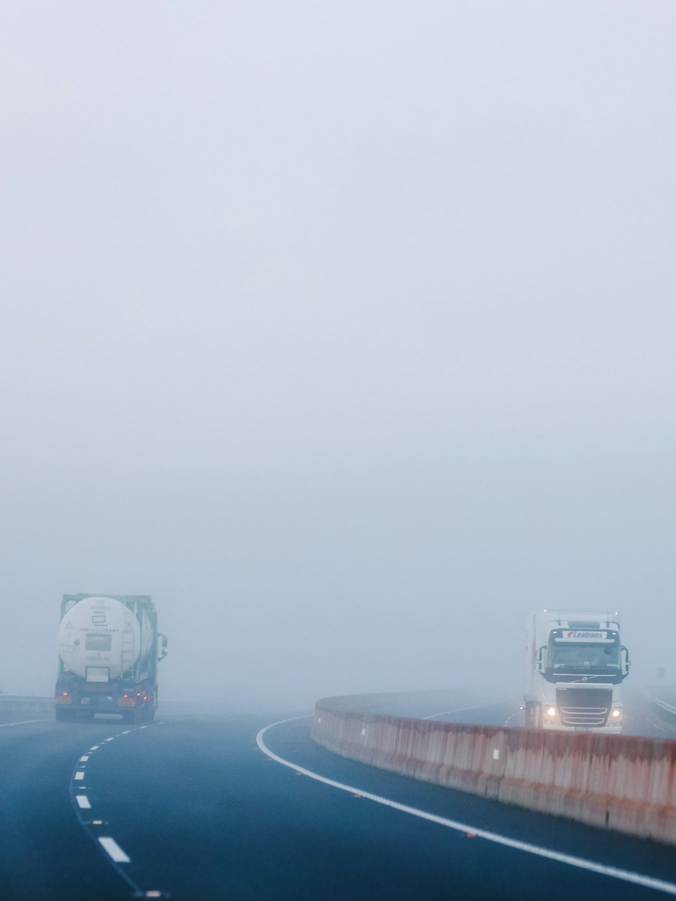Zwei Sattelzüge auf einer nebligen Autobahn hinter einer Betonschutzwand
