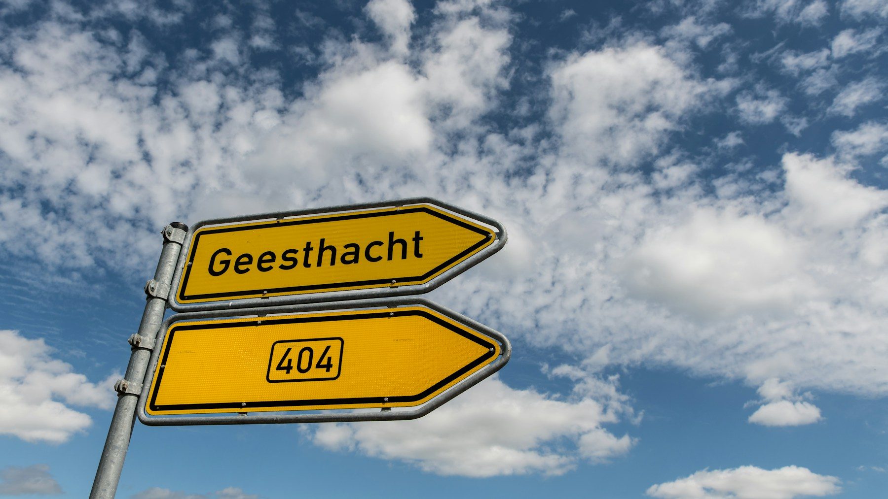Zwei gelbe Wegweiser an einem Mast, von unten gegen den Himmel fotografiert